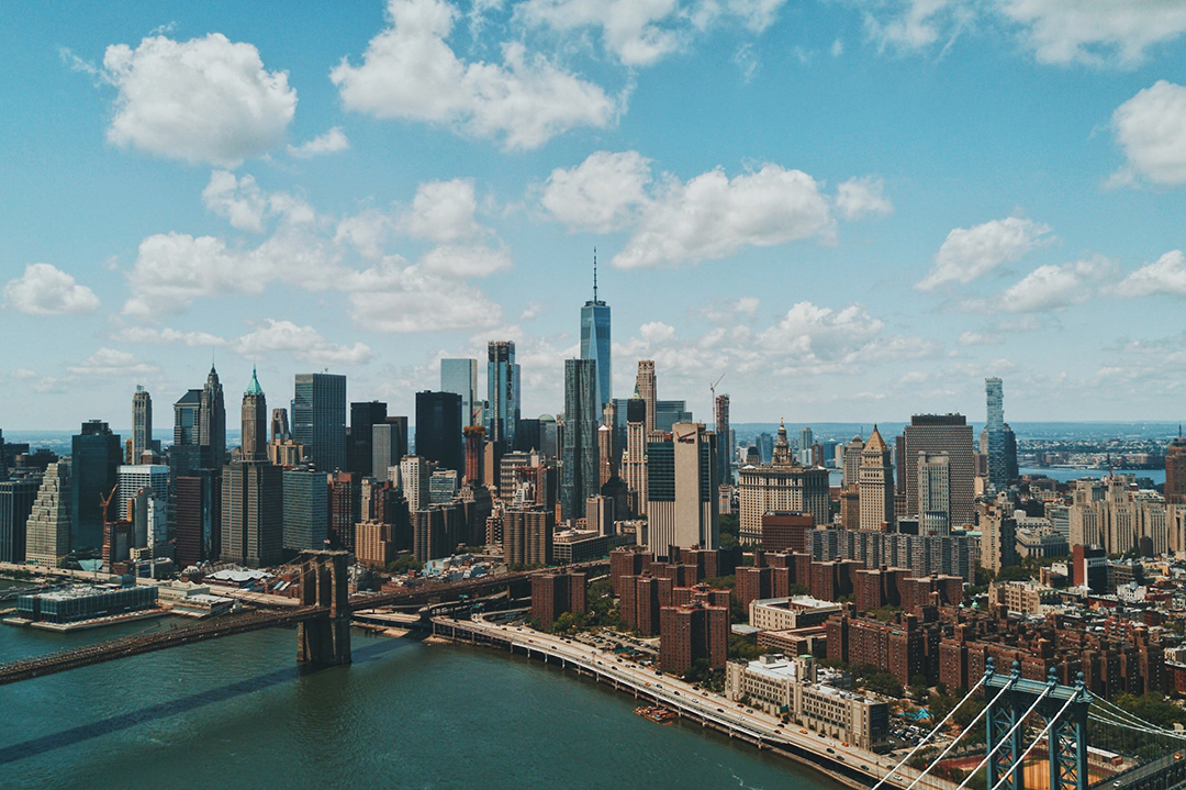 An aerial photo of New York showcasing the Manhattan Bridge, the cityscape, and a cloudy blue sky.